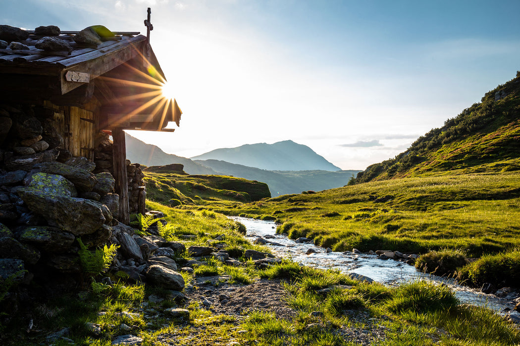 Almhütte am Bach bei Sonnenuntergang, Glasbild