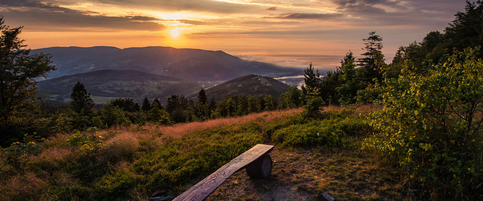 Bank auf Berggipfel bei Sonnenuntergang, Glasbild Panorama